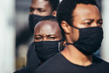 Black men on street holding masks. One of the is looking at camera with serious expression