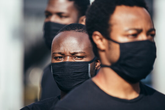 Black men on street holding masks. One of the is looking at camera with serious expression