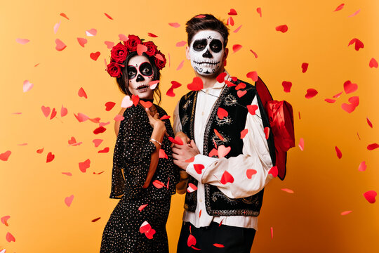 Funny Young People Dancing At Latin Party In Halloween. Studio Shot Of Couple In Masquerade Clothes Posing On Yellow Background.