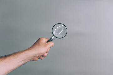 Man holds in his hand a magnifying glass on a gray background.
