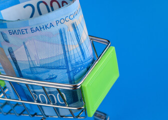 Russian rubles in a trolley on a blue background. Grocery basket and 2000 ruble bills. Russian currency. Side view. Selective focus. Copy space