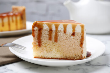 Slice of delicious cake with caramel sauce on white marble table