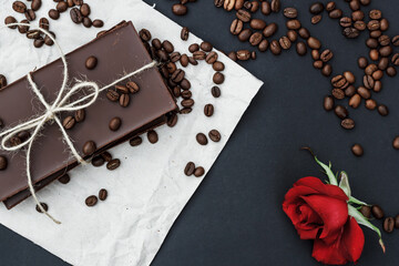 Black chocolate on a black background. Сoffe beans and a red rose are scattered in the background. Free space in the background. Image of Flat lay. World Chocolate Day.