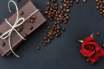 Black chocolate on a black background. Сoffe beans and a red rose are scattered in the background. 