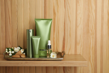 Set of cosmetic products, almond nuts and flowers on shelf near wooden wall
