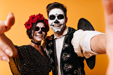 Cheerful man in sombrero making selfie with girlfriend in halloween. Funny guys with zombie makeup...