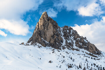 Snow covered towering mountain in the Dolomites and blue sky with clouds in winter