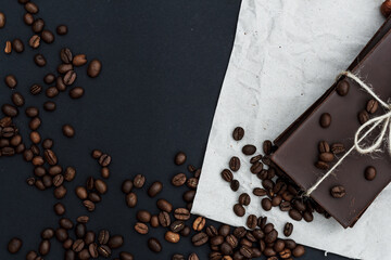Black chocolate on a black background. Сoffe beans are scattered in the background. Free space in the background. Image of Flat lay. World Chocolate Day.