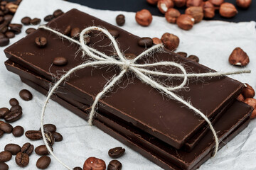Black chocolate on a black background close-up. Hazelnuts and coffe beans are scattered in the background. Free space in the background. Image of Flat lay. World Chocolate Day.