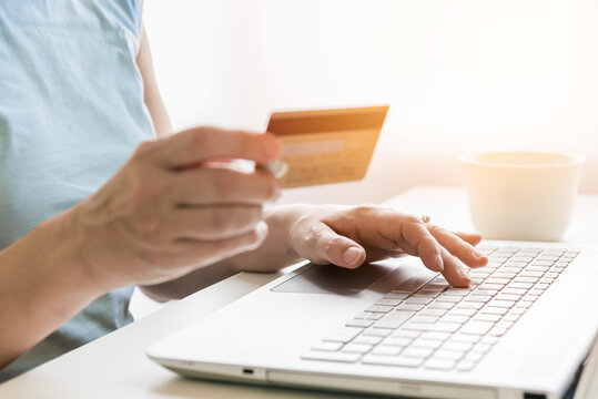 Cropped image of a woman holding a credit card while using a laptop for shopping online from home