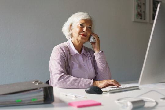 Smiling businesswoman using mobile phone while working on computer at office