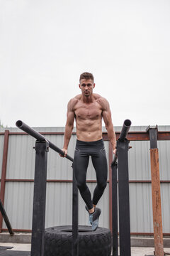 Full length of shirtless muscular male athlete exercising on parallel bars