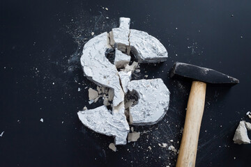 High angle view of broken concrete Dollar sign with hammer on table
