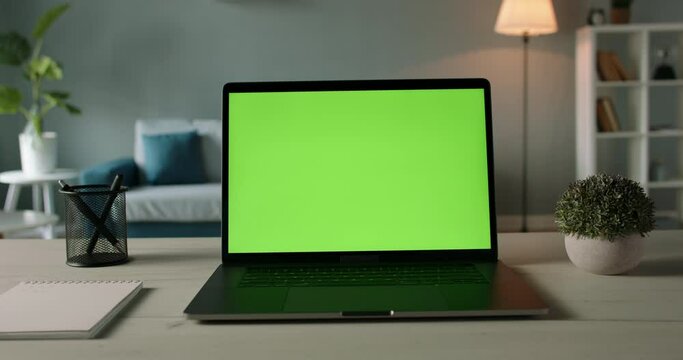 Modern laptop with mock up chroma key green screen on table of living room, desk set up for work at home - technology concept close up zoom 4k video template
