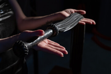 Black leather lash in the hands of an unrecognizable woman. Cropped photo of bdsms toys. Punishment...