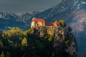 Fototapeta na wymiar Famous and beautiful castle on rock with Alps mountains in the distance. Well known landmark in Slovenia, lake Bled. Sun shining on castle in winter season