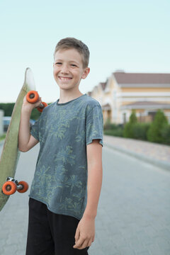 Portrait of smiling boy holding skateboard while standing on street
