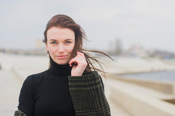 portrait of a young brown-haired girl on the city promenade, looking at the camera and holding the tip of her 