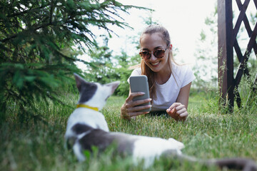 Girl in sunglasses lies on the grass and makes a photo of a cat. Outdoor recreation concept