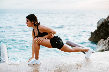 sexy athletic woman stretching exercises outdoors with sea view. Sporty attractive woman working out and stretching on beach at sunset. Female fitness model in athletic wear. Healthy lifestyle