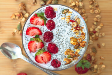 Chia pudding with raspberry chia jam in a glass garnished with strawberries, raspberries and granola. Healthy breakfast concept