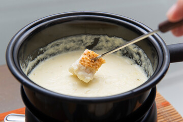 Close up of piece of bread being dipped in cheese fondue.