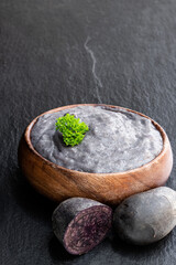 Mashed purple potatoes in wooden bowl on black stone background
