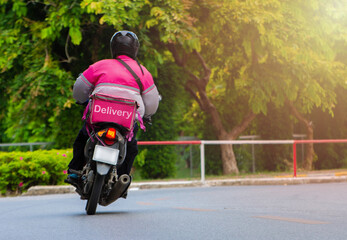 The delivery staff of the pink form uniform is driving the motorcycle to deliver the products to customers who order online.