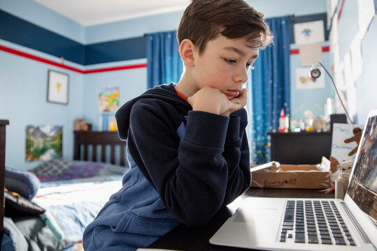 Close up of boy using laptop in bedroom