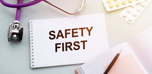 Safety first written on notebook on table with stethoscope and tablets. Medical safety and care concept