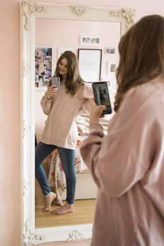 Teenage girl with smart phone taking selfie at bedroom mirror