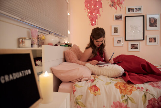 Teenage girl writing in diary on bed at home