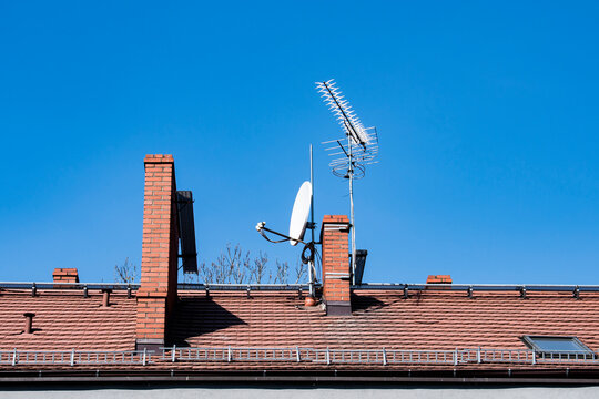 Red brick roof with chimneys and tv antennas on a clear blue sky 