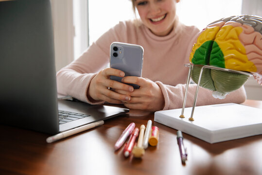 Smiling teenage girl with smart phone doing anatomy homework at home