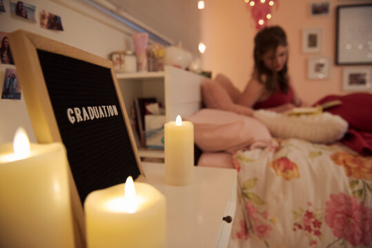Teenage girl on bed next to graduation sign and candles in bedroom