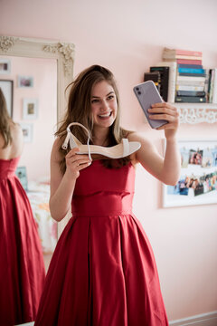 Happy teenage girl in prom dress showing shoes to friend on video chat