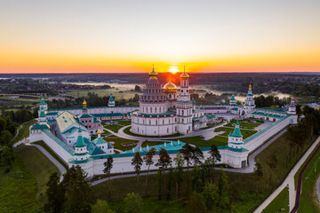 panoramic view of a white stone fortress on a green hill against the background of the rising sun, taken from a drone