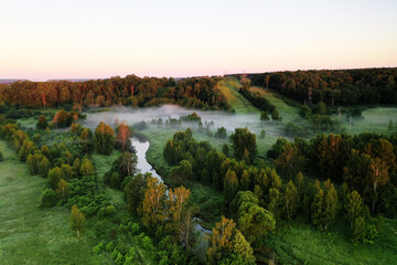 panoramic view of green meadows in the morning haze at sunrise shot from a drone at dawn