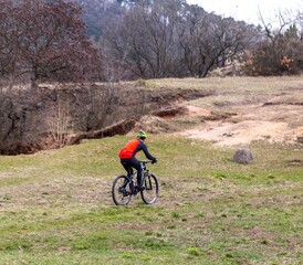 Fototapeta premium Young cyclist in red riding bike on grassy hill. Active lifestyle, extreme sport concept