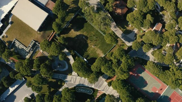 360 degree aerial footage of sport courts in the dense park with trees. People playing soccer at the court.