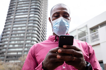 African American wearing covid19 coronavirus mask and using his smartphone in the street 