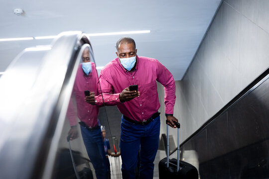 African American wearing covid19 coronavirus mask standing on escalator using his smartphone