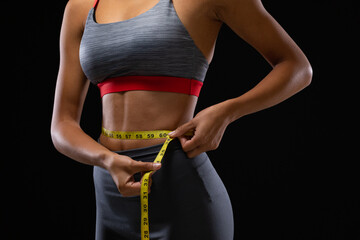 Fit mixed race woman measuring her waist with measuring tape