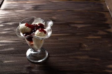 White balls of vanilla ice cream with raspberry jam in a dessert glass. Decorated ice cream on an old table made of rough wood. Copyspace.