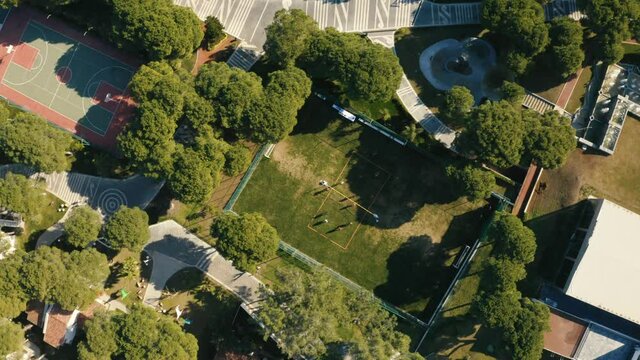 Aerial footage of sport courts in the dense park with trees. People playing soccer at the court.