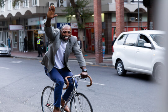 African American businessman riding a bike and greating at camera