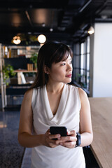 Asian woman using her phone and looking outside