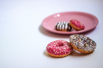 Four glazed donuts isolated on white background. Close up of two colorful donuts on white background and two small donuts on pink plate. Copy space.