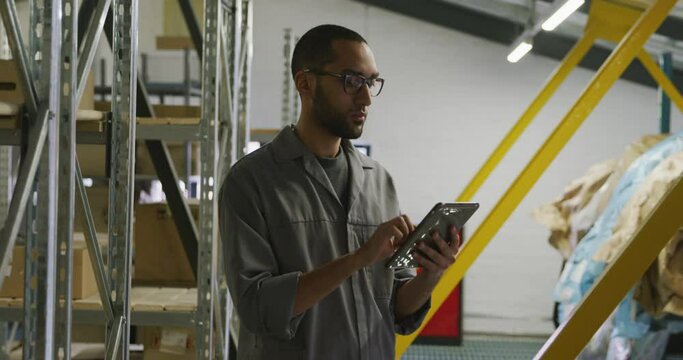 African American male car mechanic standing in a warehouse and using a tablet 