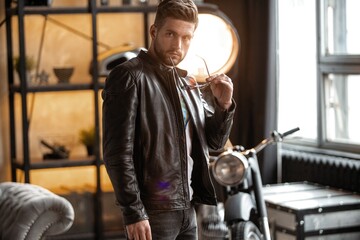 Fototapeta na wymiar Perfect man. Young hipster in leather jacket standing in room.